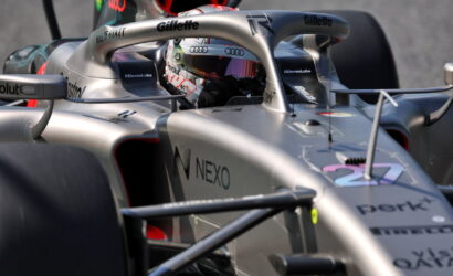Silver Formula 1 car cockpit with a driver wearing a colorful helmet, visible sponsor logos (NEXO, Gillette, Audi) and a carbon-fiber front wing in close-up view (informative image).