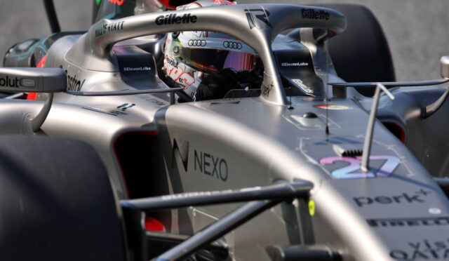 Silver Formula 1 car cockpit with a driver wearing a colorful helmet, visible sponsor logos (NEXO, Gillette, Audi) and a carbon-fiber front wing in close-up view (informative image).