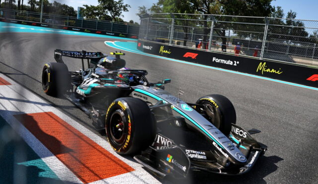Mercedes F1 car in turquoise/black livery rounds a corner on the Miami track with sponsor barriers and fencing in the background.