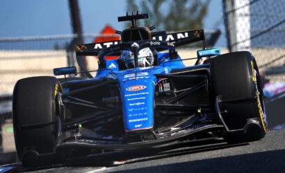 Blue Formula 1 race car on a track turning sharply, front wing and slick tires visible beneath the nose.