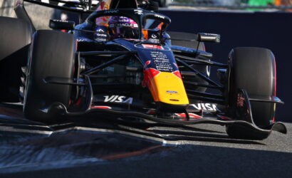 Red Bull Formula 1 car rounding a corner on the track, yellow nose and sponsor logos like Visa and Oracle visible.