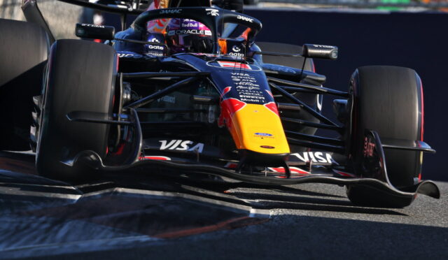 Red Bull Formula 1 car rounding a corner on the track, yellow nose and sponsor logos like Visa and Oracle visible.