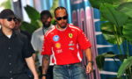 Center: man in red Ferrari shirt with sponsor logos, wearing sunglasses, walking with a security guard in black behind tropical plants.