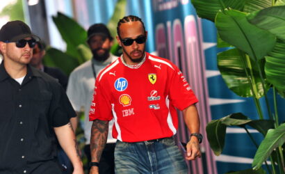 Center: man in red Ferrari shirt with sponsor logos, wearing sunglasses, walking with a security guard in black behind tropical plants.