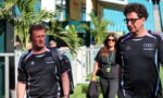 Two men in matching black athletic shirts walk through a stadium concourse, a woman in sunglasses follows behind carrying a bag and jacket.
