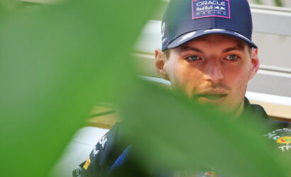 Man wearing a navy Oracle Red Bull Racing cap, looking downward, partially obscured by green leaves.