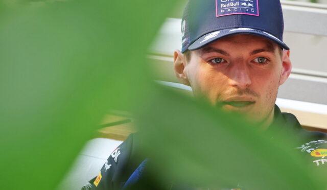 Man wearing a navy Oracle Red Bull Racing cap, looking downward, partially obscured by green leaves.