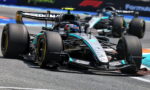 Mercedes AMG Petronas Formula One car leading a race on a sunny track with a follower close behind.