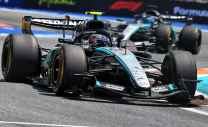 Mercedes AMG Petronas Formula One car leading a race on a sunny track with a follower close behind.