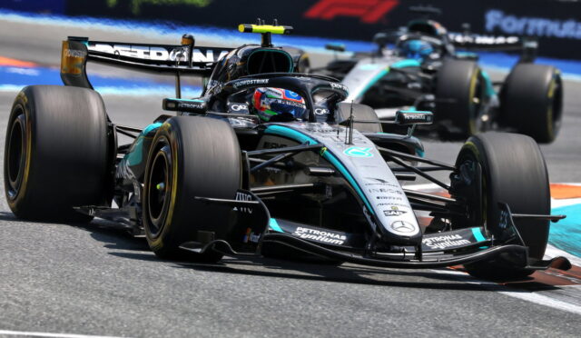 Mercedes AMG Petronas Formula One car leading a race on a sunny track with a follower close behind.