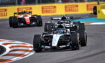 Mercedes Formula 1 car leads a pack around a bend on a race track, with yellow Pirelli barriers in the background and other F1 cars close behind.
