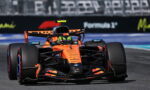 Orange Formula 1 race car speeding toward the camera on a race track, front view showing sponsor logos and bold livery.