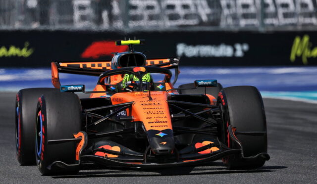 Orange Formula 1 race car speeding toward the camera on a race track, front view showing sponsor logos and bold livery.