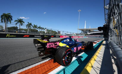 Formula 1 car in the Miami Grand Prix pit lane under a clear blue sky with palm trees in the background.