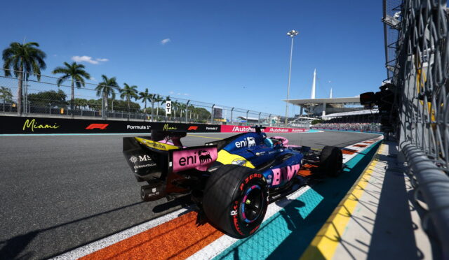 Formula 1 car in the Miami Grand Prix pit lane under a clear blue sky with palm trees in the background.