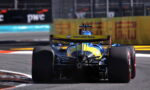 Rear view of a blue-and-yellow Formula racing car on a track, with a Mercado Libre logo on the rear wing and wide tires visible in the foreground.