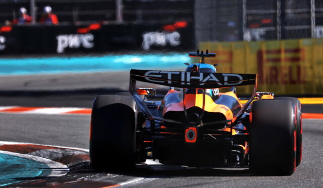 Rear view of a Formula 1 car with orange-blue livery and a large Etihad rear wing on a race track near a turn.