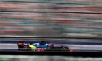 Blue and pink Formula 1 car speeding on the track with horizontal motion blur behind it, conveying high speed.