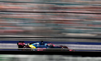 Blue and pink Formula 1 car speeding on the track with horizontal motion blur behind it, conveying high speed.