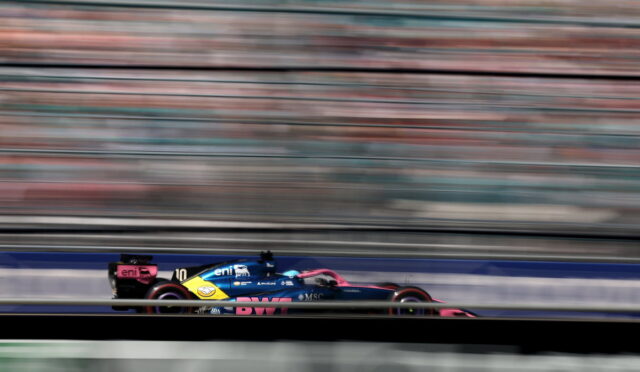 Blue and pink Formula 1 car speeding on the track with horizontal motion blur behind it, conveying high speed.