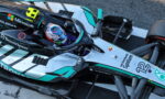 Top-down view of a Mercedes-AMG Petronas Formula 1 car on the track, cockpit visible with driver in helmet and sponsor logos nearby