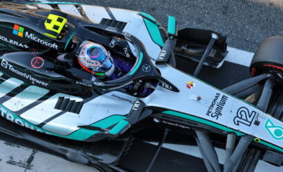 Top-down view of a Mercedes-AMG Petronas Formula 1 car on the track, cockpit visible with driver in helmet and sponsor logos nearby