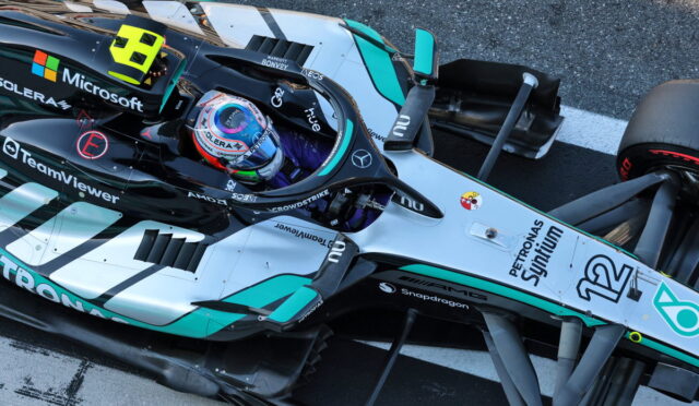 Top-down view of a Mercedes-AMG Petronas Formula 1 car on the track, cockpit visible with driver in helmet and sponsor logos nearby