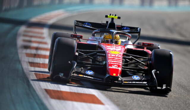 Red Formula 1 race car speeding around a track near red-and-white striped curbs, blurred background suggesting high speed in a corner on a race circuit