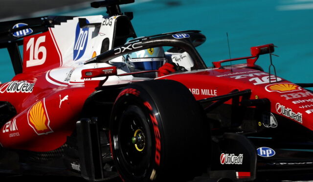 Red Ferrari Formula 1 race car on a track, driver in cockpit amid sponsor logos like Shell and Unicredit, foreground tire visible