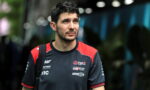 Man with short dark hair and light beard wearing a black and red esports jersey, looking to the side outdoors.
