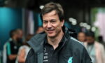 Smiling man in a dark Petronas jacket at an event, with a blurred crowd in the background.
