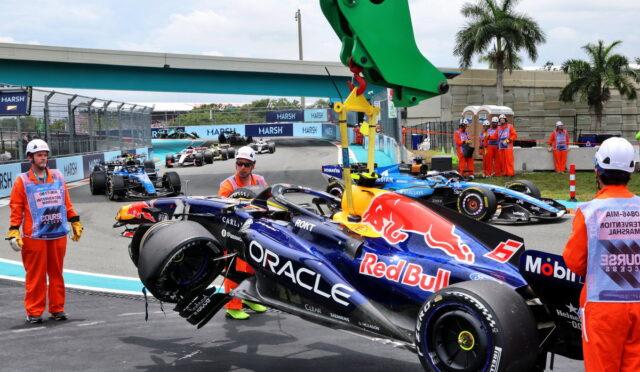 Red Bull Formula 1 car on the pit lane being lifted by a crane as crew in orange overalls watches nearby.