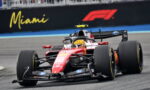 Red Ferrari Formula 1 car speeding on a race track with a Miami sign in the background.