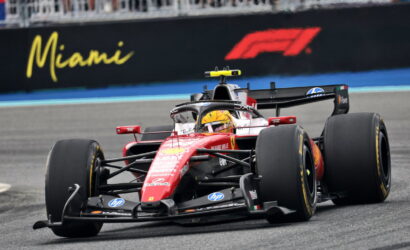 Red Ferrari Formula 1 car speeding on a race track with a Miami sign in the background.