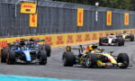 Formula 1 cars race side by side on a track with DHL banners along the barriers.