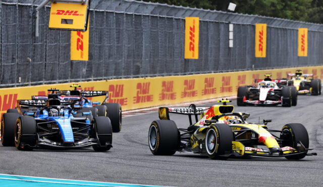 Formula 1 cars race side by side on a track with DHL banners along the barriers.
