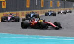 Red Formula 1 car leads a pack on a race track with DHL banners along the barriers.