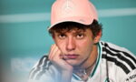 Young man wearing a pink baseball cap rests his chin on his hand, looking thoughtful toward the camera.