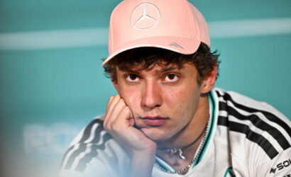 Young man wearing a pink baseball cap rests his chin on his hand, looking thoughtful toward the camera.