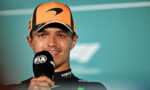 Male race driver in an orange cap speaking into a FIA microphone during a post-race interview.
