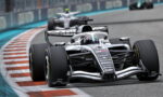 Silver Formula 1 car on a race track taking a tight corner, front wing close to the curb.