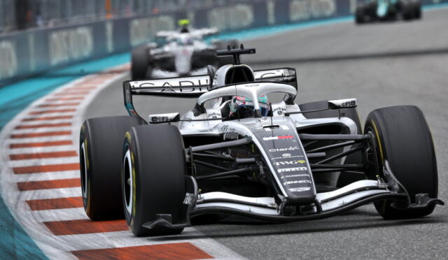 Silver Formula 1 car on a race track taking a tight corner, front wing close to the curb.
