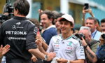Mercedes-AMG Petronas driver in a white team shirt and pink cap smiles while shaking hands with a team member amid cheering photographers and fans