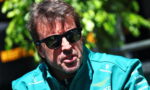 Man wearing a teal race-team jacket and black sunglasses outdoors, looking to the side.