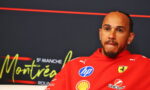 Portrait of a man in a red Ferrari jacket with sponsor logos (HP, Shell) on a dark backdrop, looking thoughtful.