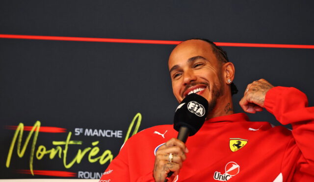 Smiling man in a red Ferrari jacket speaks into a microphone during a press interview at an event backdrop that reads Montreux.
