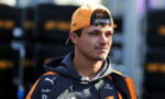 Young man in an orange cap and dark team jacket, looking to the right at a racing event.