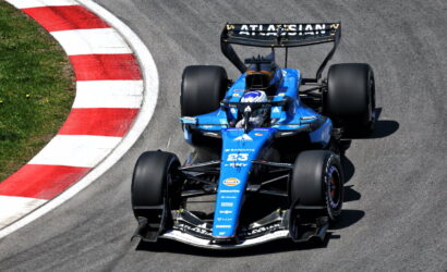 Blue Formula race car on a curved track with a red-and-white curb on the left; driver in a helmet visible inside the car.