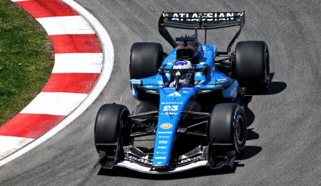 Blue Formula race car on a curved track with a red-and-white curb on the left; driver in a helmet visible inside the car.