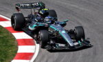 Mercedes F1 car from the Petronas team rounding a left-hand corner on a racetrack, red-and-white curbs in view